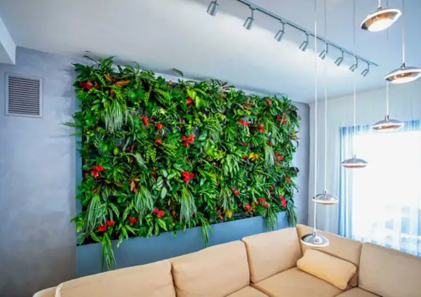 Un lussureggiante giardino verticale interno, con piante da parete verticale rigogliose e fiori rossi, domina la stanza sopra un divano beige.