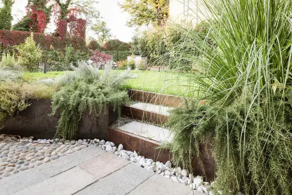 Giardino moderno con gradini in pietra e metallo corten, piante aromatiche rigogliose e ghiaia. Belle idee giardino per un'oasi verde.