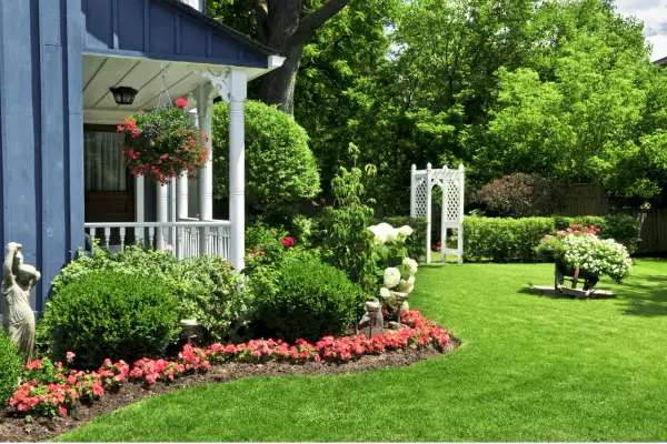 Un giardino fiorito e curato, con un portico blu e un gazebo bianco. Un'esplosione di colori dove non cresce erba, con aiuole piene di fiori rossi e bianchi.