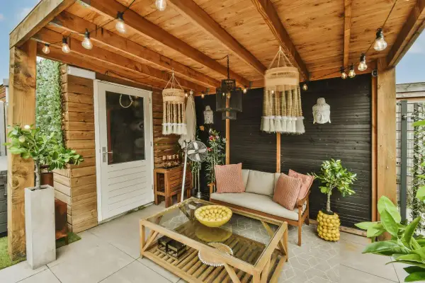 Un portico accogliente con divano, tavolino in legno e vetro, piante e decorazioni boho. Idee per come abbellire un portico con stile.