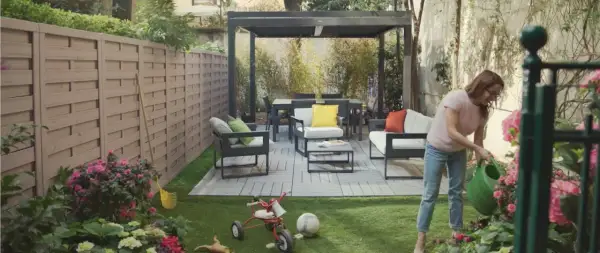 Donna annaffia fiori in un giardino moderno con mobili da esterno e un pergolato. Giardini idee da copiare per un'oasi urbana.