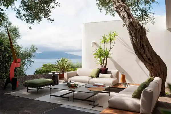 Arredare un terrazzo scoperto con divani chiari, tavolini moderni e piante rigogliose, con vista mare.